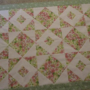 May include: A handmade quilt with a floral pattern in pink, green, and white. The quilt features a geometric design with squares and triangles. The border is a light green floral print.