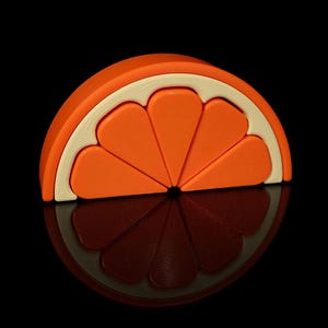 May include: A bright orange, half-circle shaped object resembling a slice of orange. The orange segment is divided into several sections, with a white rind and a dark reflection below. The background is black.