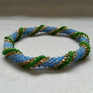 Puede incluir: Un brazalete de cuentas azul, verde y dorado con un diseño en espiral.