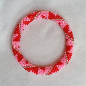 May include: A red and pink beaded bracelet with a silver thread woven throughout.