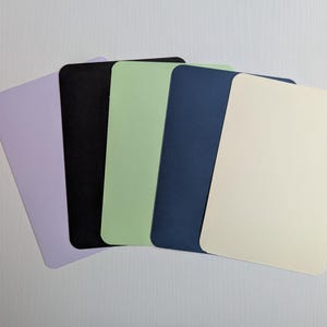 May include: A collection of five rectangular cards with rounded corners, fanned out. The cards are in shades of lavender, black, light green, navy blue, and cream. The cards are arranged on a white surface.