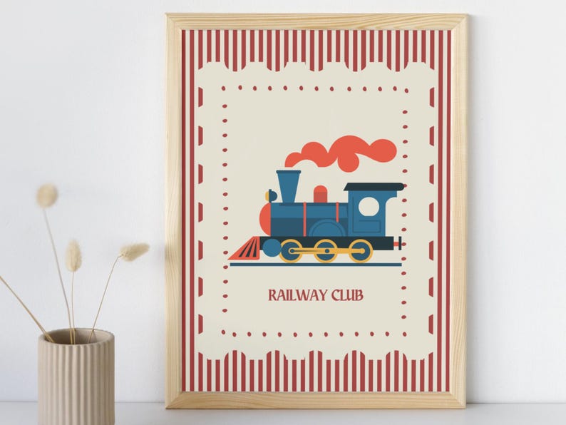 May include: A framed print featuring a blue train with orange smoke, set against a cream background. The print has a red and white striped border and the words "RAILWAY CLUB" at the bottom. The frame is made of light-colored wood.