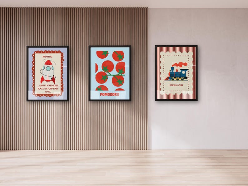 May include: Three framed art prints with black frames are displayed on a wall. The prints feature colorful illustrations: a rocket with text, tomatoes with the word "POMODORO", and a blue train with text. The wall has vertical wood paneling.