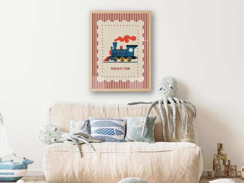 May include: A framed print featuring a blue and red cartoon train with the text "RAILWAY CLUB". The print is set against a cream background with a red border. The print is displayed above a beige sofa with decorative pillows and a stuffed octopus.