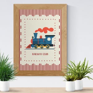 May include: A framed print featuring a blue train with red smoke, set against a cream background with a red and white border. The text "RAILWAY CLUB" is below the train. The frame is made of light brown wood.