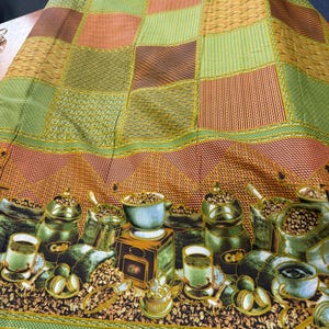 May include: A colorful fabric with a coffee theme. The top portion features a patchwork design in shades of green, orange, and brown. The bottom border showcases coffee cups, beans, and grinders in a detailed illustration. The fabric has a textured appearance.