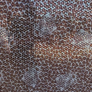 May include: Close-up of a fabric with a leopard print pattern. The fabric is covered in small, round sequins in shades of brown and silver. The sequins create a textured surface.