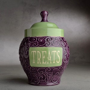 Op de afbeelding: Een groene en paarse keramische pot met een deksel en het woord "TREATS" erop.