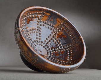 May include: A brown ceramic bowl with a textured surface and a geometric design. The bowl has a raised rim and a wide base.