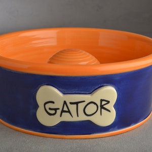 Peut inclure: Bol en céramique pour chien, orange et bleu, avec un os en forme de "GATOR".