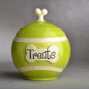 Op de afbeelding: Een groene keramische hondenkoekjespot met een wit botvormig deksel en het woord "Treats" op de voorkant.
