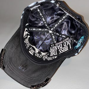Puede incluir: Una gorra de b&eacute;isbol negra vista desde el interior, con un forro de sat&eacute;n negro con un patr&oacute;n de logotipo blanco repetitivo. La banda interior para el sudor muestra el texto I MISS THE OLD DANDY HOLLYWOOD, CA en letras g&oacute;ticas blancas.