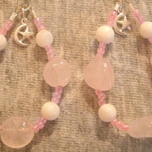 May include: A pair of pink and white beaded earrings with a silver crescent moon and star charm. The earrings feature pink and white beads and rose quartz stones.
