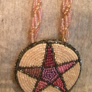 May include: A beaded necklace with a pink and beige star pendant. The star is made of small beads and has a dark gray outline.