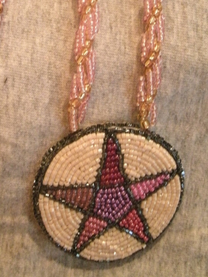 May include: A beaded necklace with a pink and beige star pendant. The star is made of small beads and has a dark gray outline.