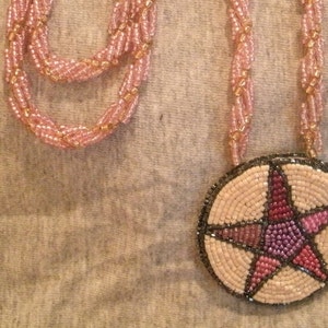 May include: A pink beaded necklace with a round pendant featuring a pink, purple, and red beaded star.