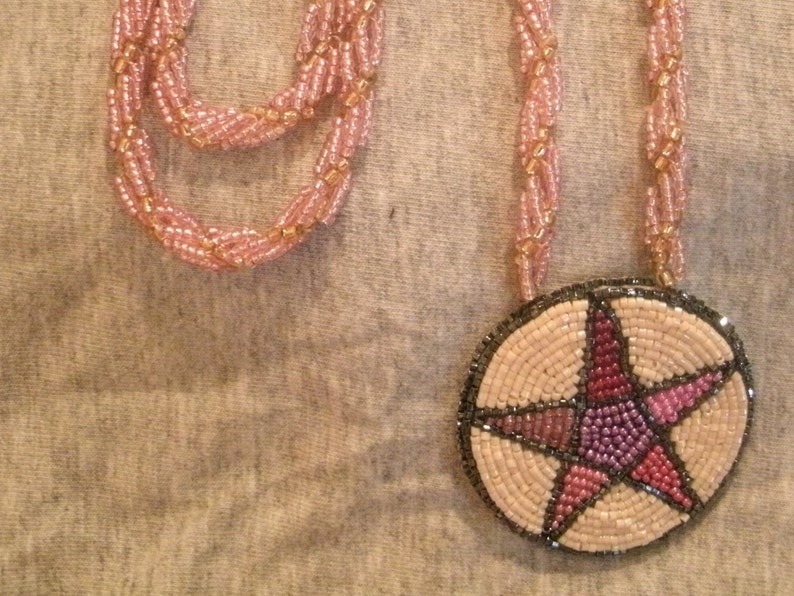 May include: A pink beaded necklace with a round pendant featuring a pink, purple, and red beaded star.