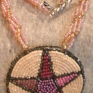 May include: A beaded necklace with a pink and gold color scheme. The necklace has a silver clasp and a pendant in the shape of a star with a pink, red, and purple design.