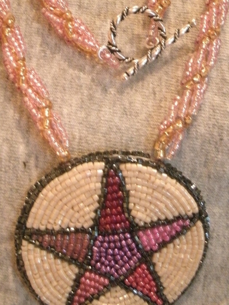 May include: A beaded necklace with a pink and gold color scheme. The necklace has a silver clasp and a pendant in the shape of a star with a pink, red, and purple design.