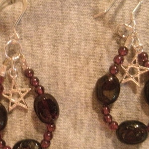 May include: A pair of dangle earrings with a silver star charm and dark purple beads.