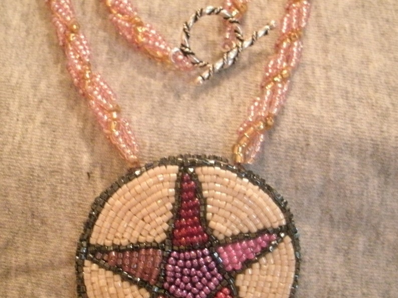 May include: A beaded necklace with a pink and gold chain and a round pendant featuring a five-pointed star in shades of pink, red, and gray.