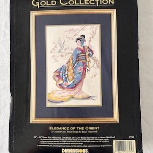 May include: A framed cross-stitch kit from The Gold Collection, featuring a woman in a kimono with cherry blossoms. The kit is titled "Elegance of the Orient" and includes a 12" x 18" frame size without mat, or 18" x 24" with mat.