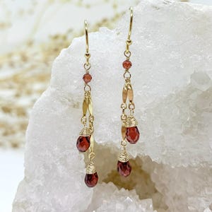 May include: Gold earrings with a dangling chain and three red garnet stones.