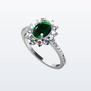 Peut inclure: Une bague en argent ornée d'une pierre précieuse ovale vert foncé au centre, entourée de pierres plus petites, claires et colorées. Le corps de la bague est également orné de petites pierres claires, créant un effet scintillant. La bague est sur fond blanc.