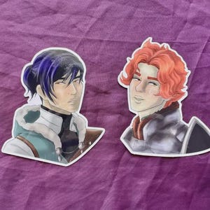 May include: Two stickers featuring illustrations of male characters. One has dark blue hair and a teal and white jacket. The other has red hair and a silver and brown jacket. Both have a white border.