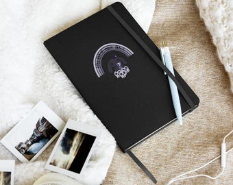 Puede incluir: Cuaderno negro con un diseño de arcoíris que dice "Like a High Back". Un bolígrafo azul claro descansa sobre el cuaderno. También se ven varias fotografías pequeñas y una cámara.