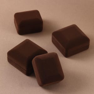 May include: Four square jewelry boxes with a dark brown velvet-like finish. Each box features a beveled lid and a compact, closed design. The boxes are arranged in a cluster, showcasing their uniform shape and deep brown color throughout the set.
