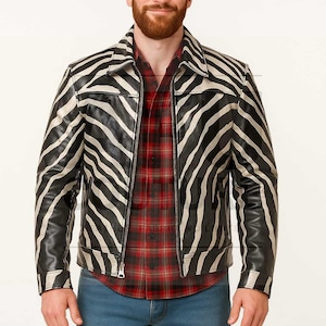 May include: A black and white zebra-striped leather jacket with a zipper closure. The jacket is worn over a red plaid shirt and blue jeans. The jacket's design features bold black stripes against a white background.
