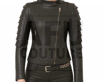 May include: Black leather jacket with a stand-up collar, asymmetrical zipper, and layered shoulder detailing. The jacket has a fitted silhouette and a studded belt. The model is wearing black leather pants.