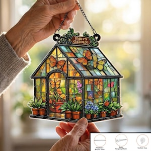 May include: A colorful, stained-glass style greenhouse decoration with the text "EMILY'S GARDEN". The acrylic piece features butterflies, flowers, and potted plants. It includes a metal hanging chain and suction cup for display.