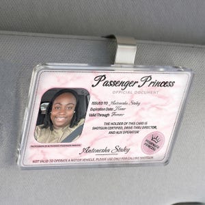 Puede incluir: Una tarjeta de visera de coche Passenger Princess de pl&aacute;stico transparente con una foto de una mujer sonriente. La tarjeta tiene un dise&ntilde;o de m&aacute;rmol rosa y el texto "Passenger Princess Official Document". Incluye el nombre "Antonesha Staley".