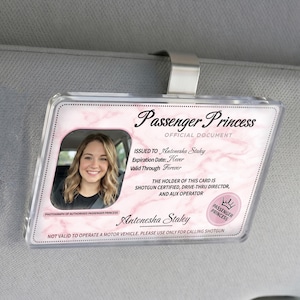 Puede incluir: Un clip de visera de coche de pl&aacute;stico transparente con una tarjeta de identificaci&oacute;n de "Passenger Princess". La tarjeta presenta una foto de una mujer sonriente, un fondo de m&aacute;rmol rosa y el texto "Shotgun Certified".
