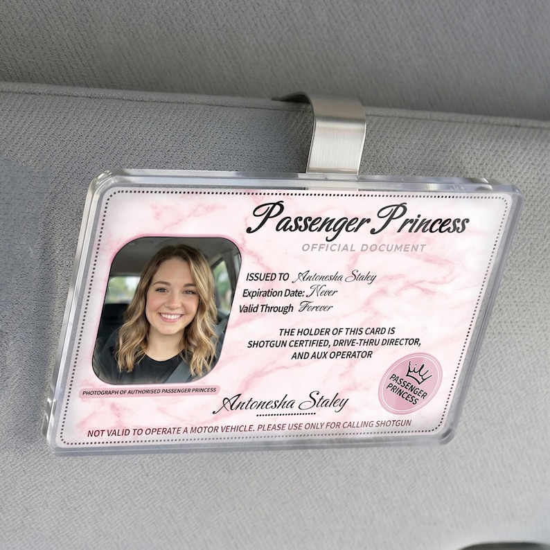 Puede incluir: Un clip de visera de coche de pl&aacute;stico transparente con una tarjeta de identificaci&oacute;n de "Passenger Princess". La tarjeta presenta una foto de una mujer sonriente, un fondo de m&aacute;rmol rosa y el texto "Shotgun Certified".