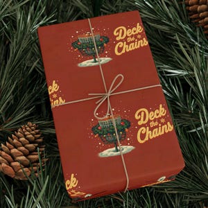 May include: Red wrapping paper with a repeating pattern of a disc golf basket decorated for Christmas, with the text "Deck the Chains" in gold. The paper is tied with twine and set on a bed of pine needles and pine cones.