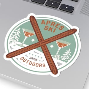 Pode incluir: Um autocolante redondo com as palavras "APRES SKI" e "DRINK OUTDOORS" num estilo vintage. O autocolante apresenta esquis cruzados, copos de cocktail e uma cena de montanha nevada. O autocolante está num portátil.