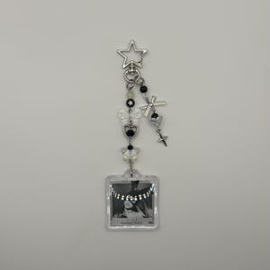 May include: A silver keychain with a star-shaped clasp, adorned with black and white beads, bows, and charms. A small, clear square pendant features a black and white image with the text "DANGEROUS WOMAN".