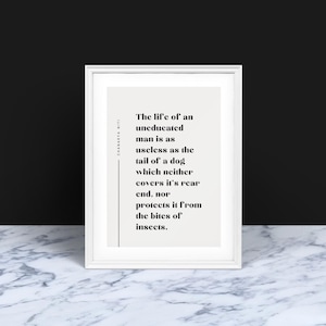 Op de afbeelding: Een ingelijste print met een witte rand, met een citaat in zwarte tekst op een lichtbeige achtergrond. Het citaat luidt: "Het leven van een ongeschoolde man is zo nutteloos als de staart van een hond die noch zijn achterste bedekt, noch hem beschermt tegen insectenbeten."