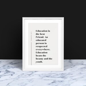 Op de afbeelding: Een witte lijst met de tekst "Onderwijs is de beste vriend. Een geschoold persoon wordt overal gerespecteerd. Onderwijs overtreft schoonheid en jeugd." De print staat tegen een lichtbeige achtergrond. De lijst staat op een marmeren oppervlak.
