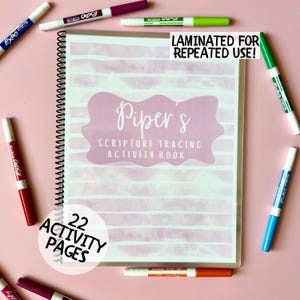May include: A spiral-bound activity book titled "Piper's Scripture Tracing Activity Book" with 22 activity pages. The cover features a pink watercolor design and the text "Laminated for Repeated Use!". Several colorful dry-erase markers surround the book on a pink background.