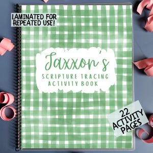 May include: A spiral-bound activity book with a green and white gingham pattern cover. The cover features the text "Jaxxon's Scripture Tracing Activity Book" in a white cloud-shaped text box. A small sticker indicates "22 Activity Pages". The book is laminated for repeated use.