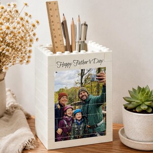 Peut inclure: Un porte-crayons rectangulaire blanc fabriqué à partir de blocs de construction en plastique emboîtables. L'avant présente une photo imprimée d'une famille et le texte Happy Father's Day. Il contient trois crayons et une règle en bois.