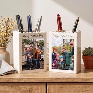 May include: Two white rectangular pen holders constructed from interlocking plastic building blocks. Each holder features a custom printed photograph on the front and the text Happy Father's Day. Several pens are stored inside each container.