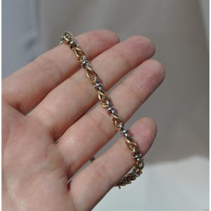 May include: A gold and silver bracelet with an intricate woven design. The bracelet features alternating gold-toned woven links and silver-toned connecting beads. The jewelry is held in a hand against a neutral background.