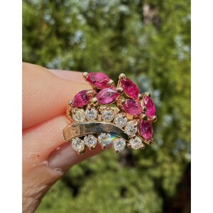 May include: A gold ring featuring a cluster of marquise-cut pink gemstones and round white diamonds. The ring has a unique design with multiple layers and a polished gold band. The gemstones are set closely together, creating a vibrant and eye-catching display.