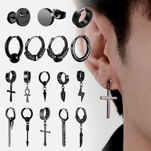 Könnte beinhalten: Eine Sammlung schwarzer Ohrringe in verschiedenen Stilen, darunter Creolen, Stecker und Hängeohrringe. Designs umfassen Totenkopf, Kreuz, Ankh, Feder und Blitz. Einige Ohrringe sind an einem Ohr zu sehen.