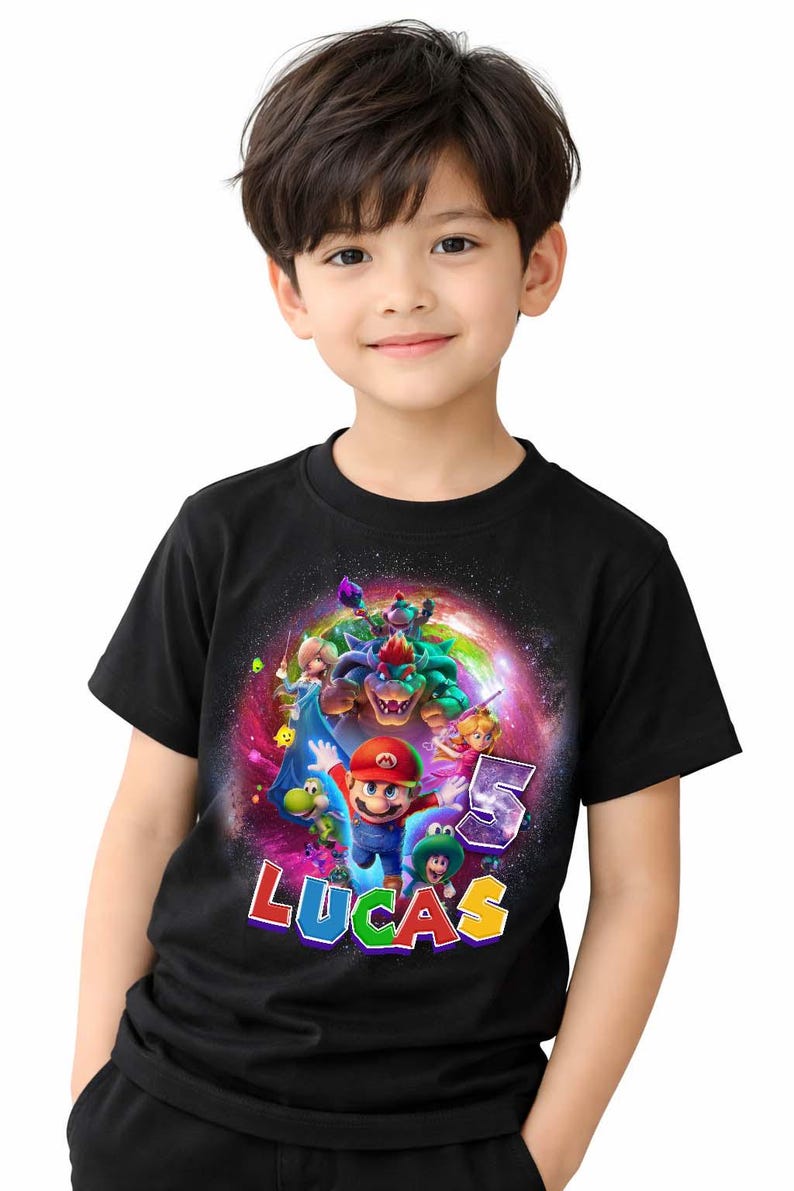 Puede incluir: Camiseta negra con un dise&ntilde;o colorido de Mario y otros personajes de Super Mario. El dise&ntilde;o incluye el n&uacute;mero "5" y el nombre "LUCAS". La camiseta la lleva un ni&ntilde;o peque&ntilde;o.